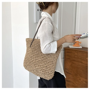 Detail of hand-woven straw shoulder bag in khaki with brown leather straps for summer beach use