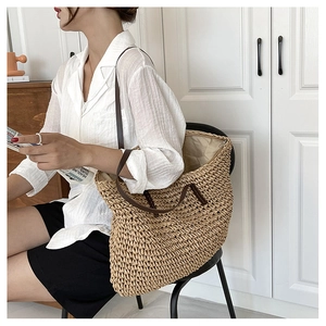 Detail of a large woven straw tote bag with brown leather straps worn by a model