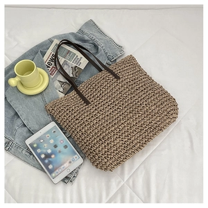 Top view of woven straw tote bag with brown leather handles on white bedding