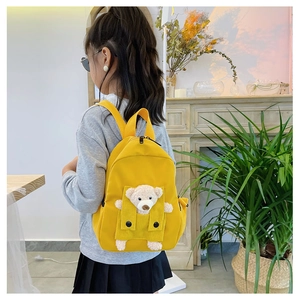 Bambino che indossa uno zaino in tela giallo brillante con un simpatico orsetto