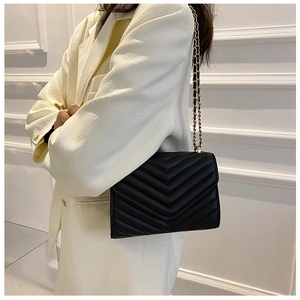 Side view of woman wearing a black quilted leather crossbody bag with gold chain strap