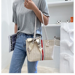 Detail of beige straw beach tote bag featuring thick rope handles and silk scarf accent