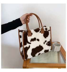 Detailed view of plush cow print tote bag with brown leather handles and reinforced edges