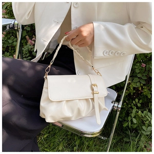 Detail of cream pleated handbag with woven handle and gold buckle on a model