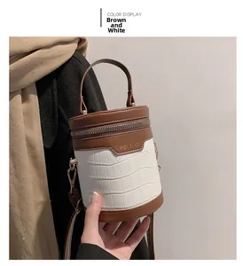 Detail der weißen Zylindertasche mit Krokodilmuster und braunen Lederakzenten und Griff