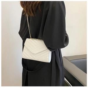 Model wearing a white quilted crossbody bag with gold chain strap and V-stitch design