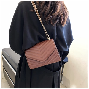 Close-up of brown crossbody bag with chevron quilting and golden chain strap detail