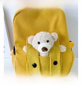 Dettaglio dello zaino giallo per bambini con un orsetto di peluche nella tasca anteriore
