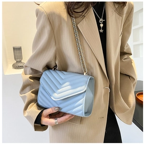 Detail of light blue quilted crossbody bag with V-shaped stitching and chain strap