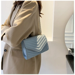 Light blue crossbody bag with V-shaped quilting and gold chain strap on model