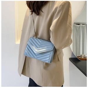Blue V-quilted small square bag with metal chain strap worn on a beige blazer