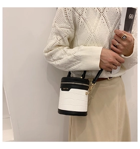 Detail der weißen Zylindertasche mit Krokoprägung, schwarzem Besatz und Kettenriemen