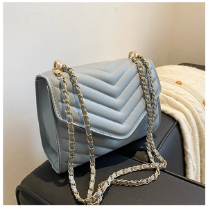 Detail of light blue quilted crossbody bag featuring elegant gold metal chain strap