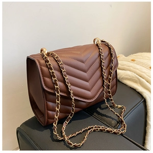 Detail of dark brown quilted leather shoulder bag with gold chain strap on a textured surface