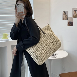 Large cream woven straw tote bag with brown leather straps shown on shoulder