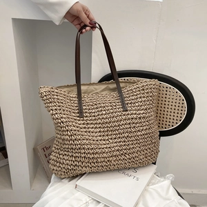 Large beige woven straw tote bag with brown leather handles for beach or summer vacation