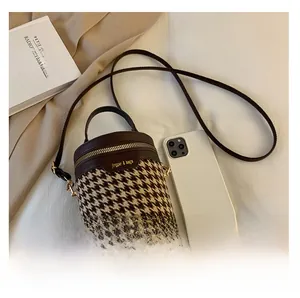 Detailed view of houndstooth cylinder bucket bag with leather accents and gold hardware