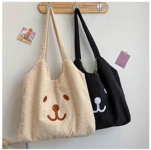 Détail de sacs fourre-tout en peluche brodés en beige et noir sur crochets en bois