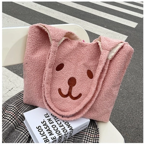 Détail d'un sac cabas rose en peluche avec un visage d'ours brodé posé sur une chaise