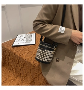 Detail of houndstooth tweed bucket bag with black leather trim and golden zipper
