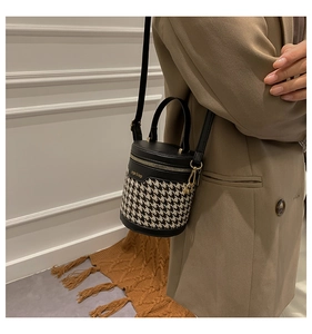 Detailed view of houndstooth cylinder bucket bag with black leather trim and gold hardware
