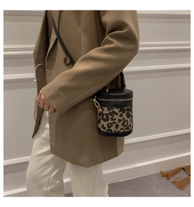 Detail of leopard print cylinder bucket bag featuring gold metal hardware and black leather trim
