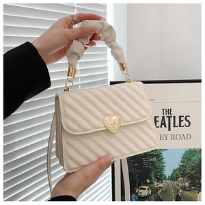 Detail einer cremefarbenen Stepptasche mit goldenem Herzverschluss und Falten-Griff