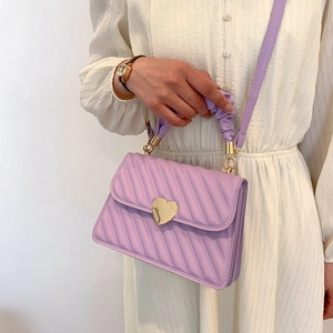 Detail der lila gesteppten Schultertasche mit goldener Herzschnalle und Haargummi-Griff