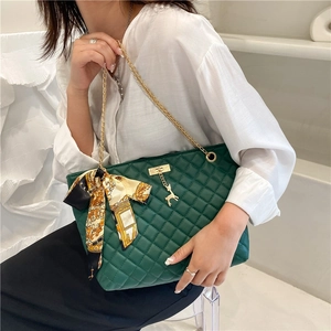 Detailed view of dark green quilted shoulder bag with gold chain and silk scarf bow
