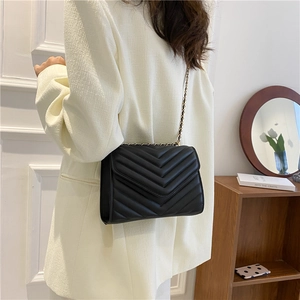 Women's black V-quilted faux leather chain crossbody bag worn with a white blazer