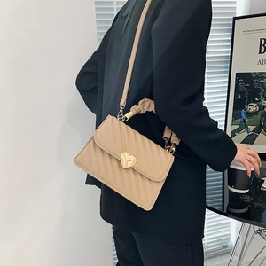 Quilted beige shoulder bag with gold heart clasp and dual straps worn by a model