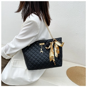 Close-up of a black quilted shoulder bag with a silk scarf bow and gold chain strap.