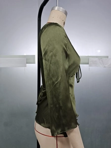 Close-up of dark green satin shirt featuring bell sleeves and waist tie detail