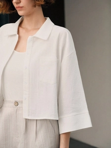 Minimalist white cropped cotton shirt with long sleeves and breast pocket on white background