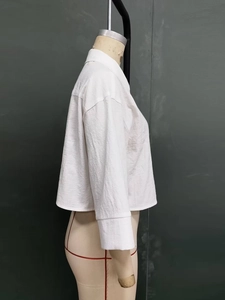 Detail showing the textured cotton fabric and dropped shoulder of a white cropped shirt