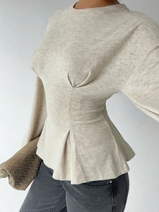Close-up of oatmeal knit long sleeve top with peplum waist and textured fabric detail