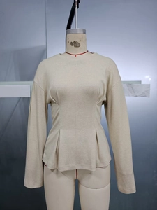 Detail of off-white long sleeve knit top with pleated waist and flared hem design