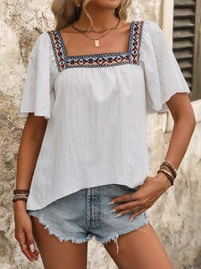 Detail of colorful geometric embroidery on the square neckline of a white boho blouse
