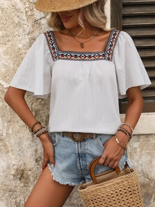 Close-up of geometric embroidery and square neckline on a white bohemian blouse