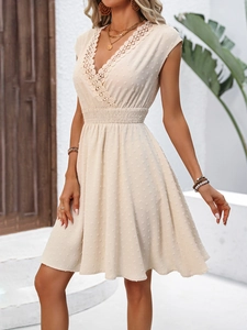 Detailed view of the deep V-neck lace trim and Swiss dot fabric on cream dress