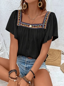Close-up of square neckline featuring colorful ethnic embroidery on a black summer blouse