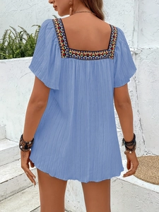 Close-up of geometric embroidery on a blue square neck blouse for a summer look
