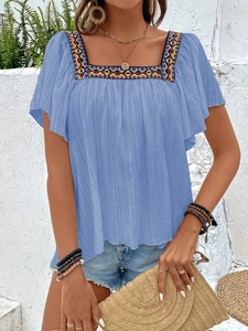 Detail of square neckline with colorful ethnic embroidery and ruffle sleeves on blue blouse
