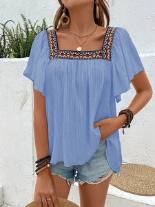 Close-up of geometric embroidery on a light blue square neck boho top with ruffle sleeves