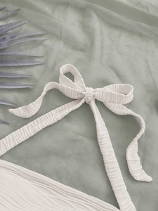 Detail of the tied bow shoulder strap on a textured beige summer beach camisole top