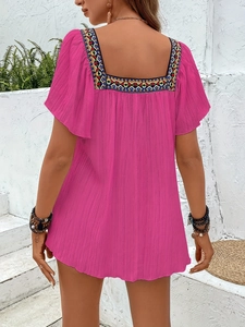 Detail of rose pink blouse featuring colorful geometric embroidery and square neckline