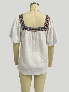 Close-up of colorful geometric embroidery on a white square neck shirt with ruffles