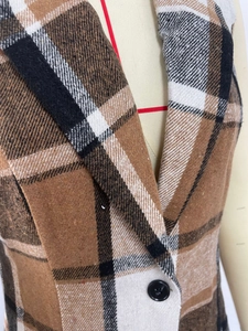 Gros plan sur le tissu à carreaux marron du gilet avec col à revers et bouton noir