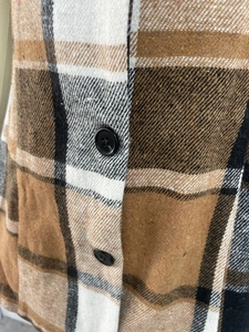 Gros plan sur le tissu à carreaux marron et le bouton noir de ce gilet pour femmes