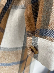 Detailed close-up of plaid flannel shirt cuff with button and warm brushed fabric texture